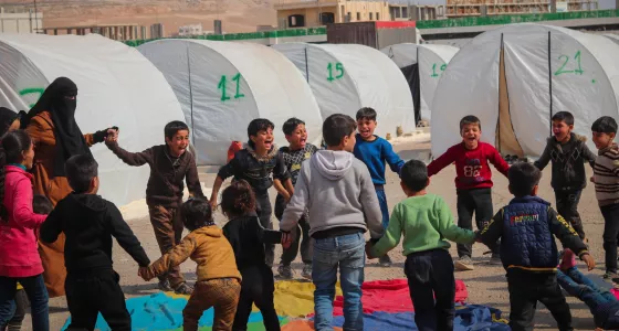 Children holding hands in a circle in a refugee camp in Syria around a colourful parachute