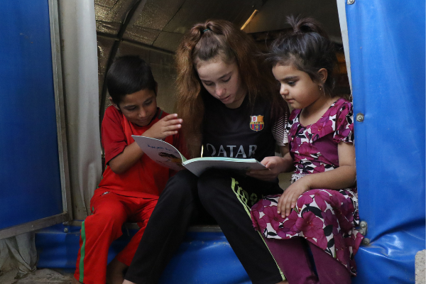 Participant Nadia reading to her siblings in their home in a displacement camp in Iraq.