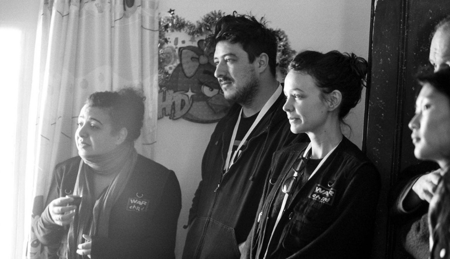 Carey Mulligan and Marcus Mumford standing together and talking to War Child programmes staff.