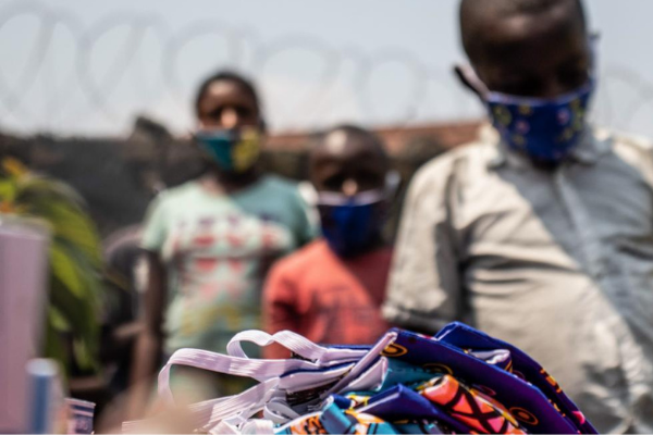 Children in the DRC stand socially distanced wearing masks whilst they await COVID-19 kits from War Child.