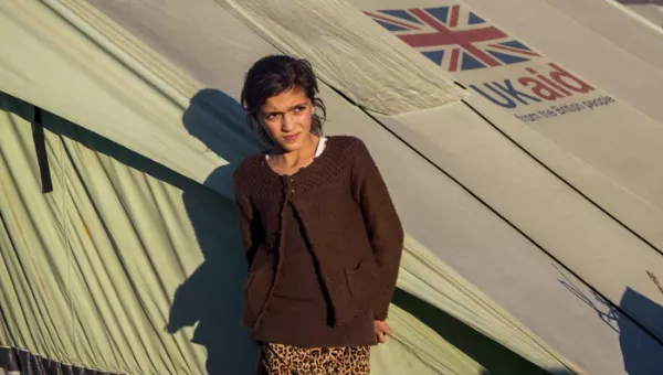 Girl in front of a tent bearing the UK Aid logo in a displacement camp.