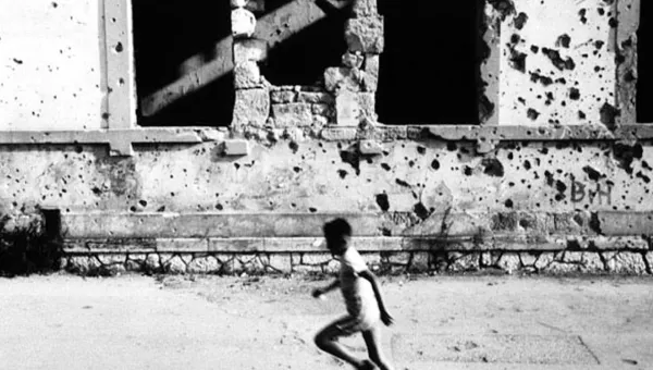 Child running in front of building damaged by conflict in Mostar, Bosnia.