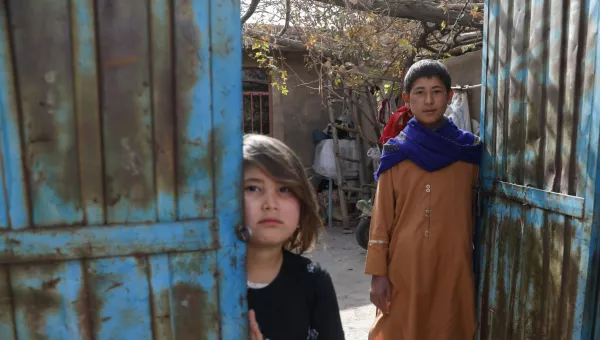 Participant Hassan and his little sister stand outside their home in Afghanistan.