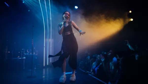 Griff performing on stage at Lafayette. The lighting is blue and yellow shining on a crowd who are singing along. Griff is singing and caught in a half twirl on stage.