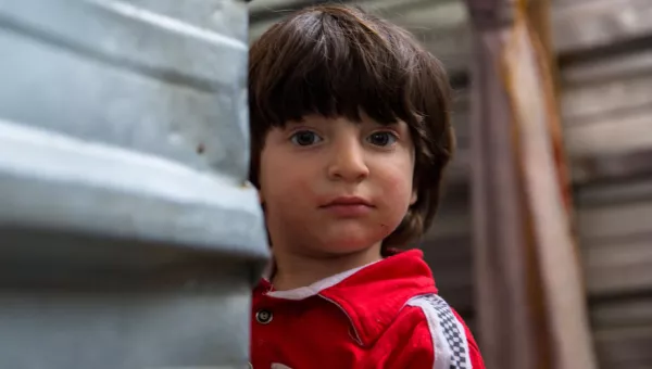 Iraqi boy peeps round the corner of a shelter in a displacement camp in Iraq.