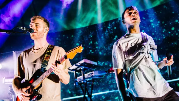 Tom Misch playing his guitar on stage surrounded by blue and green lighting. 