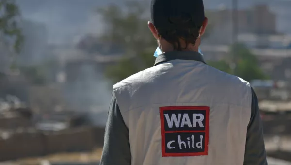 War Child staff member stands with back to camera showing jacket with War Child logo on their back.