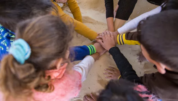 Children in Jordan put their hands into the middle of their circle as they play games at a child-friendly space.