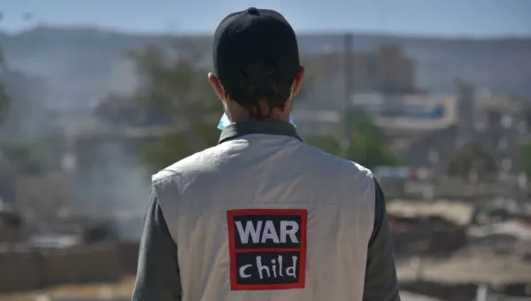 War Child staff member stands with back to camera showing jacket with War Child logo on their back.