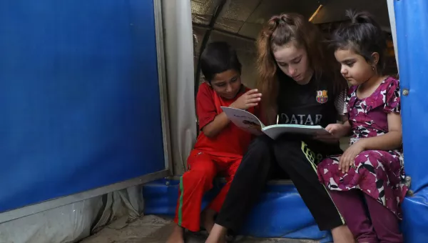 Participant Nadia reads to her siblings at their home in a displacement camp in Iraq.