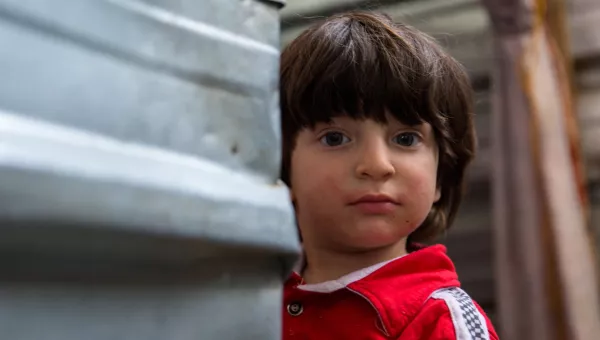 Iraqi boy peeps round the corner of a shelter in a displacement camp in Iraq.