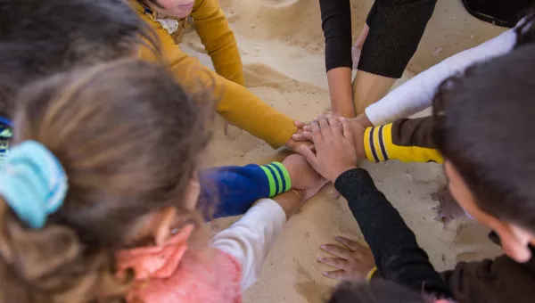 Children in Jordan put their hands into the middle of the circle as they play at a War Child child-friendly space in Jordan.