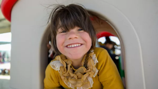 Girl smiling as she plays outside a War Child child-friendly space.