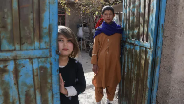 Participant Hassan and his little sister stand outside their home in Afghanistan.