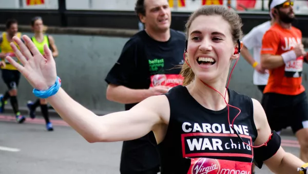 A Team War Child runner waving whilst completing the London Marathon.
