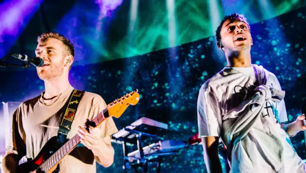 Tom Misch playing his guitar on stage surrounded by blue and green lighting. 