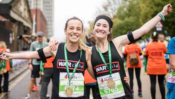 Two Team War Child runners celebrate with their medals at the Royal Parks Half finish line.