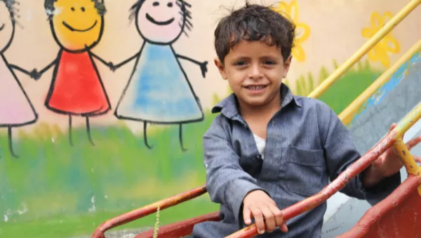 Participant sits on a slide outside a War Child child-friendly space in Yemen.