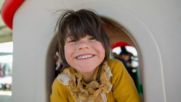 A child smiling whilst playing outside a child-friendly space.