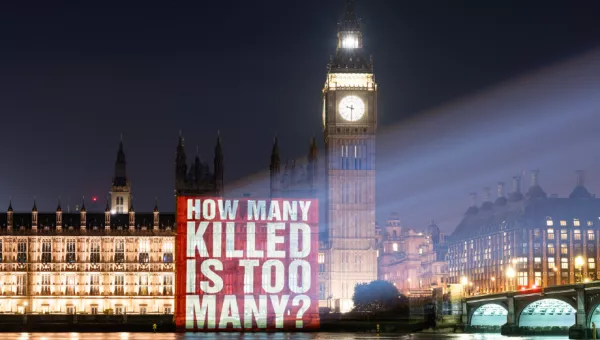 A light projection on the side of Parliament that says HOW MANY KILLED IS TOO MANY? in white lettering on a red background