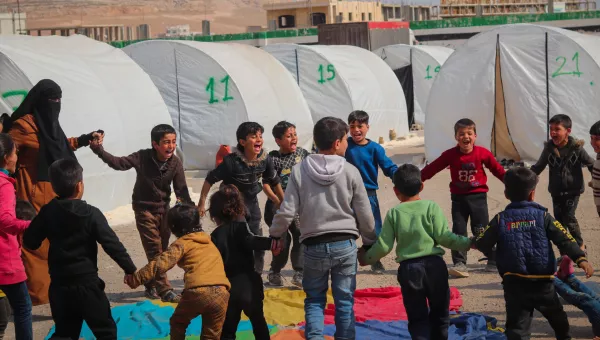 Children holding hands in a circle in a refugee camp in Syria around a colourful parachute