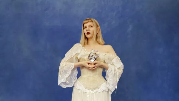Aurora standing in front of blue wall in a white dress holding a metal heart