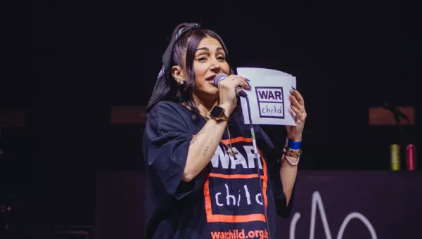 Ellie Prohan standing on stage wearing a War Child t-shirt. 