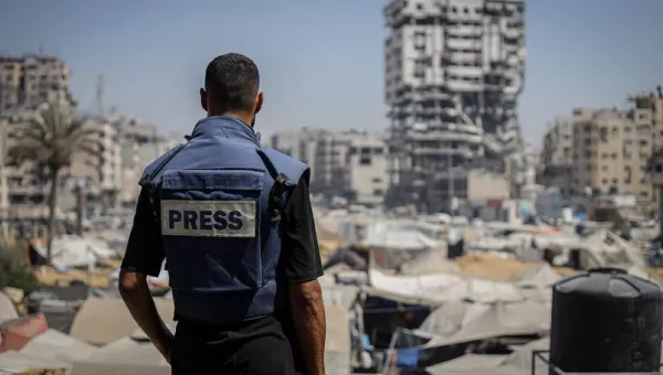 A member of the press standing wearing a press vest looking out to Gaza.