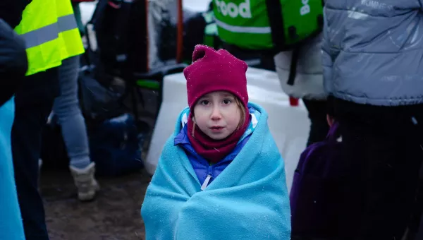 Little girl looking at camera. She is wrapped in a blue blanket and is wearing a red scarf and hat.