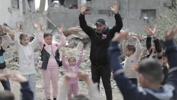 An adult man and children standing amongst rubble with hands in the air