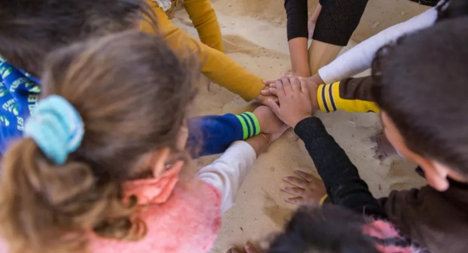 Children in a War Child child-friendly space in Jordan put their hands in together before playing a game. Photo: Rosie Lyse Thompson