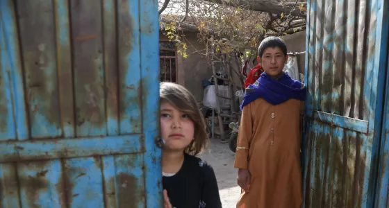 Participant Hassan and his little sister stand outside their home in Afghanistan.