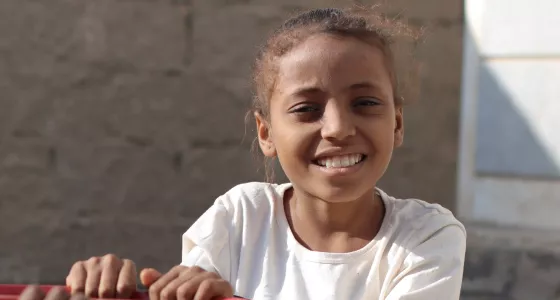 Little girl in Yemen plays on equipment outside a child-friendly space.