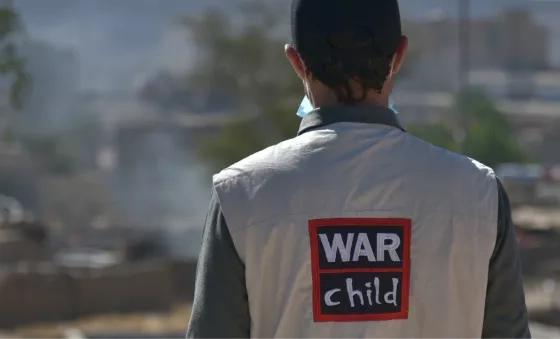 War Child staff member stands with back to camera showing jacket with War Child logo on their back.