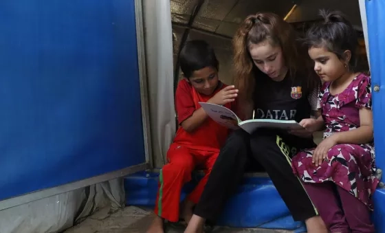 Participant Nadia reads to her siblings at their home in a displacement camp in Iraq.