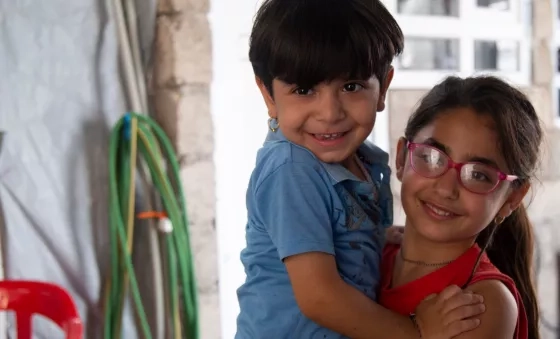 Participant Soleen carries her younger brother in their home.