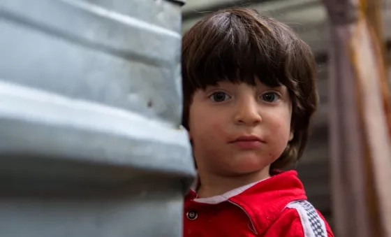 Iraqi boy peeps round the corner of a shelter in a displacement camp in Iraq.