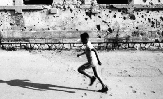 A child running in front of a damaged building covered in bullet holes in Mostar, Bosnia.