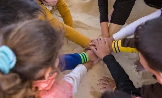 Children in Jordan put their hands into the middle of the circle as they play at a War Child child-friendly space in Jordan.