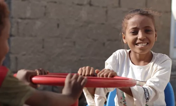Little girl in Yemen plays on equipment outside a child-friendly space.