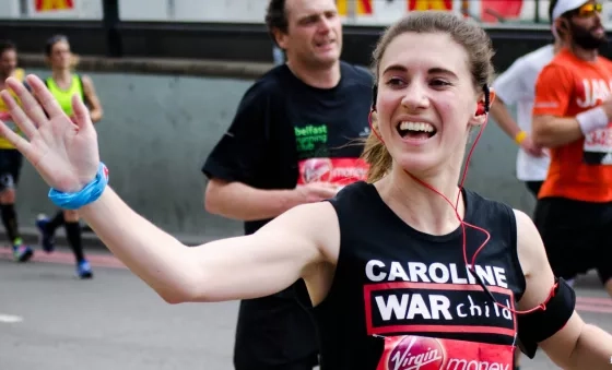 Team War Child runner Caroline waves whilst running part the War Child cheer point at the London Marathon.