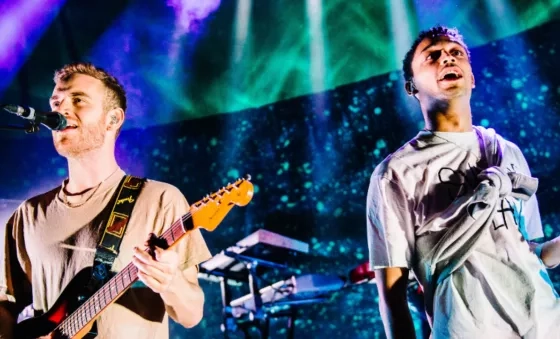 Tom Misch playing his guitar on stage surrounded by blue and green lighting. 