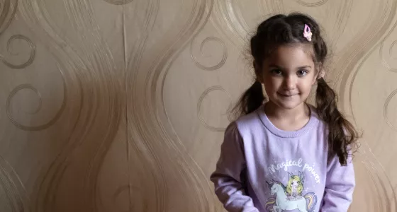 Girl in purple unicorn top standing against a wall in her home