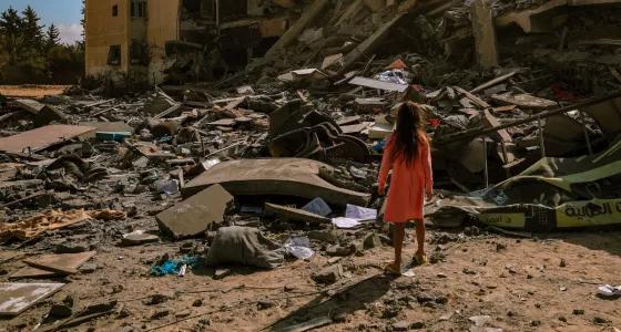 A girl standing in front of a collapsed building in Gaza.