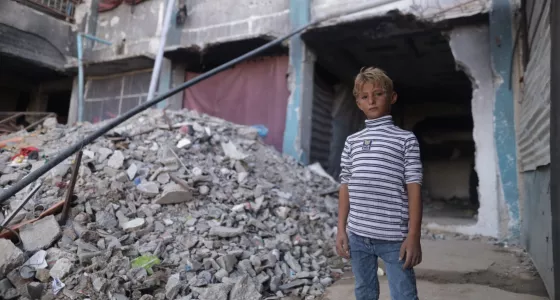 Boy standing next to a collapsed building in Gaza.