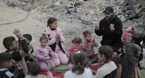 A War Child staff member sits surrounded by children amongst rubble in Gaza