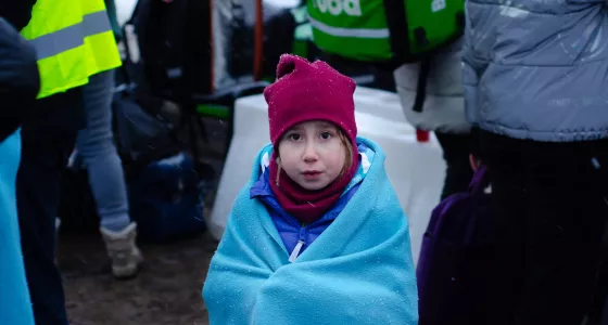 Little girl looking at camera. She is wrapped in a blue blanket and is wearing a red scarf and hat.