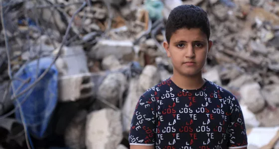 boy stands in front of rubble looking at camera