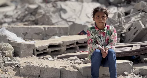 girl sits amongst rubble looking at camera