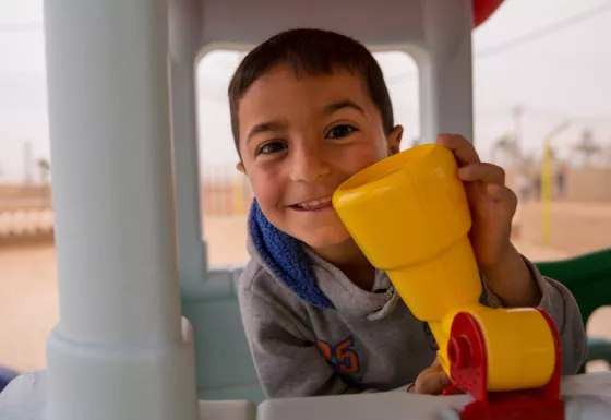 Boy plays in playhouse outside of a War Child child-friendly space.